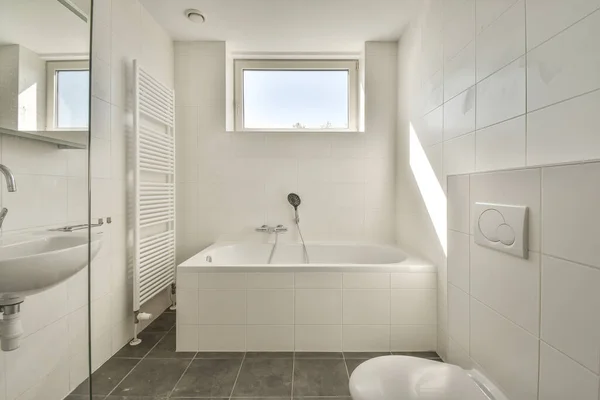 Modern home interior design of white bathroom with open bathtub and shower separated from toilet by partition wall