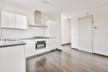 Pencereleri ve ahşap parke zemini olan boş beyaz mutfağın içi.