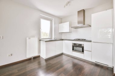 Pencereleri ve ahşap parke zemini olan boş beyaz mutfağın içi.