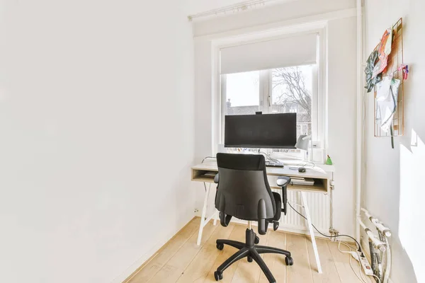 Minimalist narrow interior of study room with parquet floor and white walls furnished with settee and table with computer