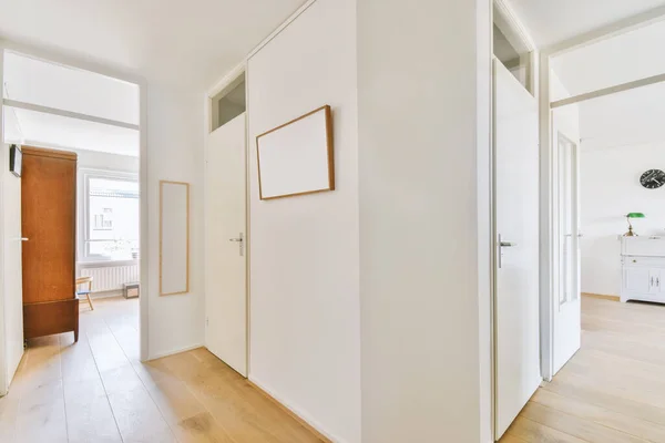 白い壁とドアを持つ狭い廊下は 現代のアパートの窓や寄木細工の床と広々とした部屋につながります — ストック写真