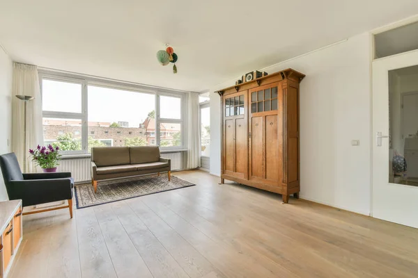 Shabby wooden table with chairs and vase located near comfortable couch against light walls with decorations and TV in modern apartment