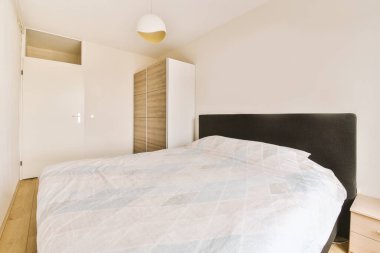 Cam kapının yanına yerleştirilmiş süslü battaniyeli rahat yatak ve aydınlık yatak odasındaki aynalı gardırop.