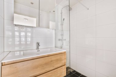 Modern banyoda aynalı lavabo ve cam kapılı duş kutusu ve beyaz fayanslı duvarlar.