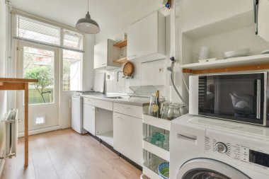 Çağdaş mutfaktaki beyaz dolaplarla tezgahların üzerine çeşitli mutfak malzemeleri ve aletler yerleştirilmiş.