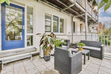 Parlak tuğla balkon, metal parmaklıklar, tahta sandalye ve kapı.