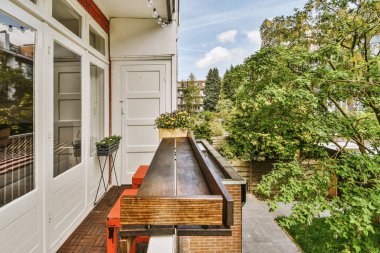 Narrow brick balcony with metal railings, wooden chair and door