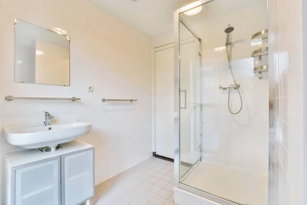 Interior of modern bathroom with rectangular mirror and clean sinks attached to white tiled wall near shower box in modern washroom