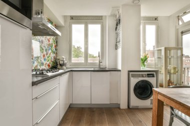 Stüdyo dairesinin modern minimalist tarzı iç tasarımı açık beyaz mutfak ve yemek masası ve sandalyeleri tavan arası lambasıyla aydınlatılmış.