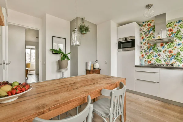 Modern minimalist style interior design of studio apartment with open white kitchen and dining zone with table and chairs illuminated by loft style lamp