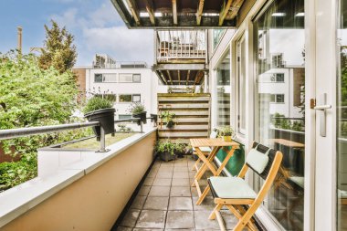 Dar tuğlalı balkon, metal parmaklıklar, tahta sandalye ve kapı.