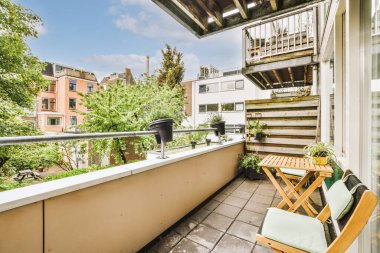 Narrow brick balcony with metal railings, wooden chair and door