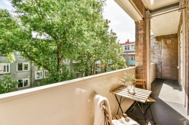 Dar tuğlalı balkon, metal parmaklıklar, tahta sandalye ve kapı.