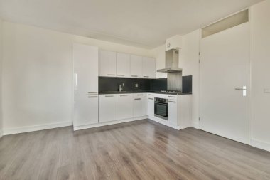 Pencereleri ve ahşap parke zemini olan boş beyaz mutfağın içi.