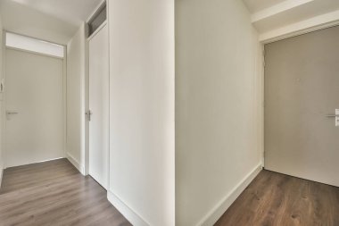 Giriş kapısı, beyaz duvarları ve parke zemini lambayla aydınlatılmış, geometrik tasarımı olan boş, modern bir daire.