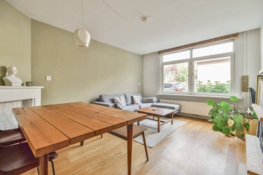 Büyük pencerenin yanında halısı ve bej koltuğu olan basit pahalı bir oturma odası.