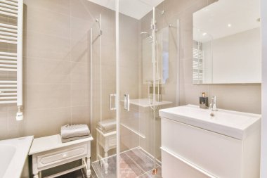 Aynalı lavabo ve temiz küvet modern banyoda cam kapılı ve beyaz fayanslı duvarları olan duş kutusunun yanında.