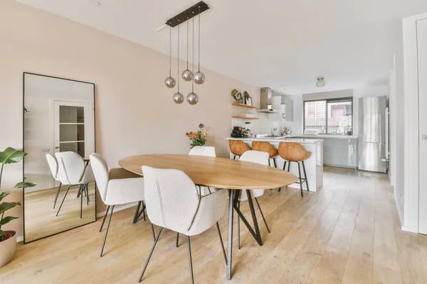 Modern minimalist style interior design of studio apartment with open white kitchen and dining zone with table and chairs illuminated by loft style lamp