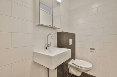 Duvara asılmış tuvalet ve köşedeki bej fayanslı lavabo.