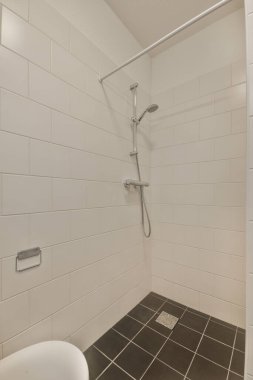 Evdeki modern tuvalette asılı duran banyo musluğu ile duvar arasındaki cam bölme.