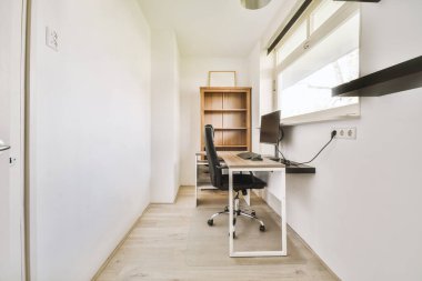 Modern apartmandaki hafif iş yerinde bilgisayar monitörleri ve beyaz tahtanın olduğu masanın yanına konforlu sandalye