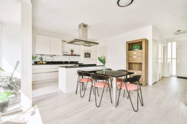 Stüdyo dairesinin modern minimalist tarzı iç tasarımı açık beyaz mutfak ve yemek masası ve sandalyeleri tavan arası lambasıyla aydınlatılmış.