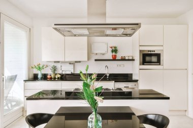 Stüdyo dairesinin modern minimalist tarzı iç tasarımı açık beyaz mutfak ve yemek masası ve sandalyeleri tavan arası lambasıyla aydınlatılmış.