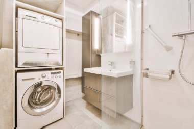 Sinks with mirrors with washing machine and shower box with glass door in modern bathroom with white tiled walls