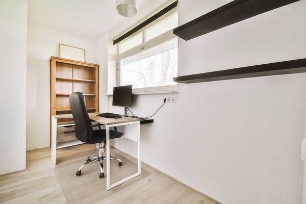 Comfortable chair placed near desk with computer monitors and whiteboard in light workplace in modern apartment