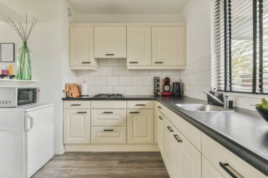 İyi organize edilmiş küçük bir ev mutfağı pencerenin altında lavabo, sobalı hafif mobilyalar ve kentsel apartmanda buzdolabı var.