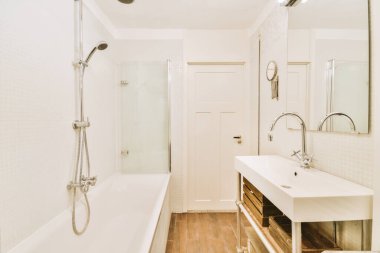 Aynalı lavabo ve temiz küvet modern banyoda cam kapılı ve beyaz fayanslı duvarları olan duş kutusunun yanında.