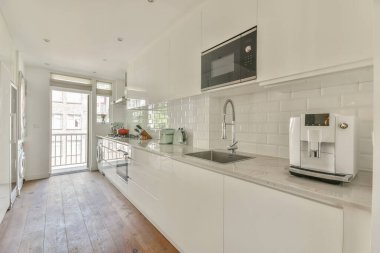 Beyaz oturma odasında açık siyah mutfak, yemek masası ve gri kanepe.