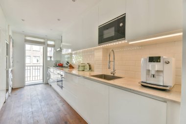 Beyaz oturma odasında açık siyah mutfak, yemek masası ve gri kanepe.