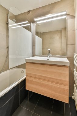 Çağdaş dairenin küçük fayanslı banyosunda lavabo ve duş arasında bulunan sifon tuvaleti