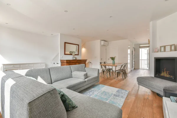 Beyaz oturma odasında açık siyah mutfak, yemek masası ve gri kanepe.