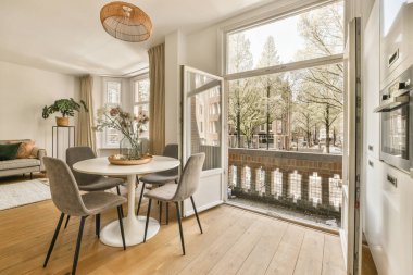 Çağdaş dairenin geniş odasındaki dinlenme odası ve mutfağın yakınındaki sandalyeli ve çiçekli masa.