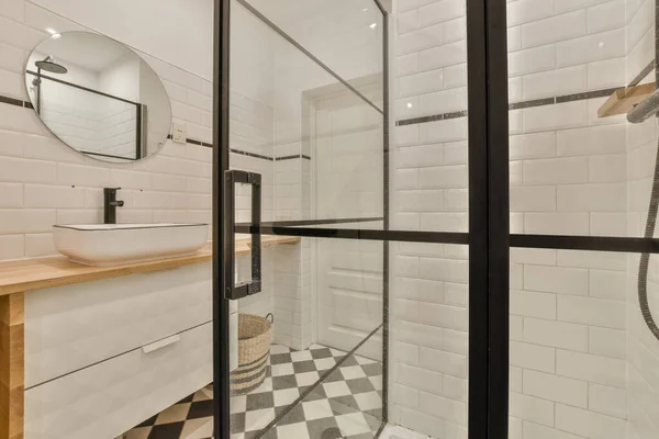 Interior of modern bathroom with rectangular mirror and clean sinks attached to white tiled wall near shower cabin in modern washroom