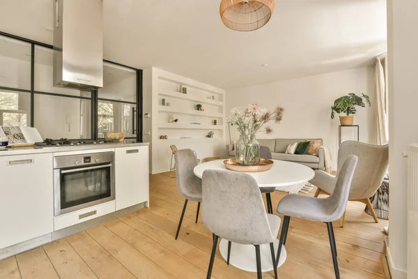 Çağdaş dairenin geniş odasındaki dinlenme odası ve mutfağın yakınındaki sandalyeli ve çiçekli masa.