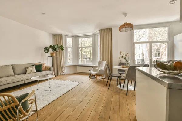 Çağdaş dairenin geniş odasındaki dinlenme odası ve mutfağın yakınındaki sandalyeli ve çiçekli masa.