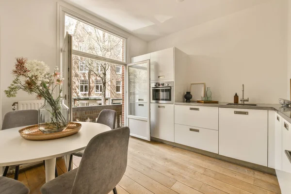 Çağdaş dairenin geniş odasındaki dinlenme odası ve mutfağın yakınındaki sandalyeli ve çiçekli masa.