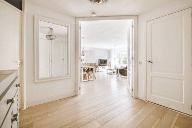 Beyaz duvarları ve kapıları olan dar koridor modern dairede pencereleri ve parke zemini olan geniş odaya açılıyor.