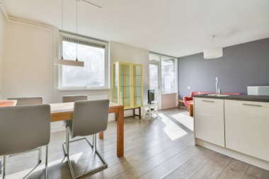 Çağdaş dairenin geniş odasındaki dinlenme odası ve mutfağın yakınındaki sandalyeli ve çiçekli masa.