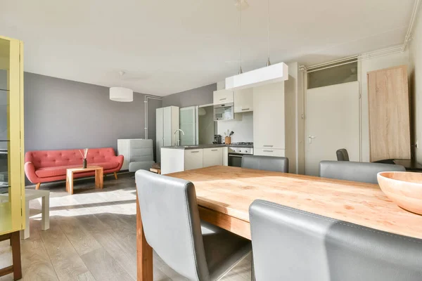Table with chairs and flowers located near lounge area and kitchen in spacious room of contemporary apartment