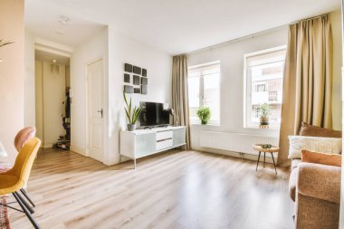 Geniş pencereli, ahşap kanepeli, dolaplı ve televizyonlu modern minimalist oturma odasının iç tasarımı beyaz duvara yerleştirilmiş.