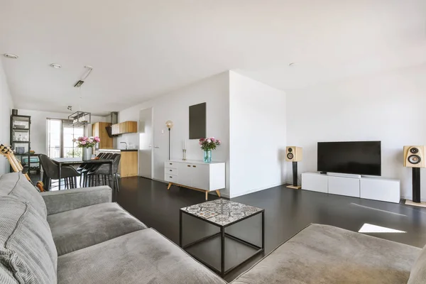 Contemporary minimalist style interior design of light studio apartment with wooden table and chairs in dining zone between open kitchen and living room with white walls and parquet floor