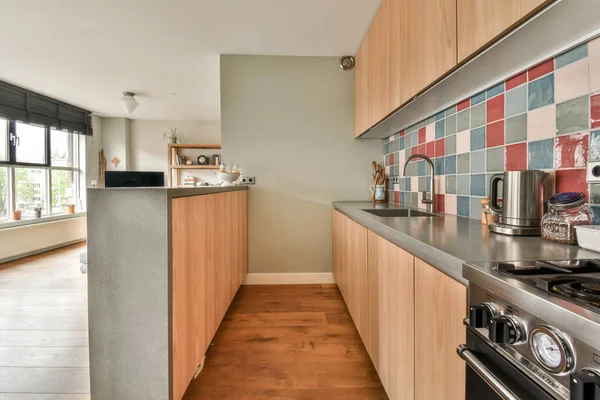 Well organized small home kitchen interior with sink under window and light furniture with stove and fridge in urban apartment