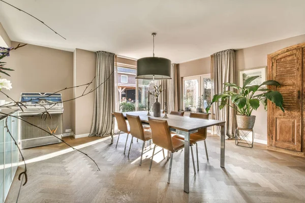 Modern minimalist style interior design of studio apartment with open white kitchen and dining zone with table and chairs illuminated by loft style lamp