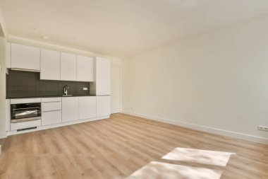 Pencereleri ve ahşap parke zemini olan boş beyaz mutfağın içi.