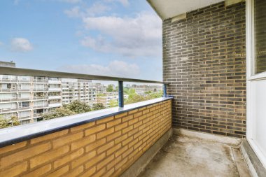 Metal parmaklıklı dar tuğla balkon, tahta sandalye ve camlı kapı mutfağa açılıyor.