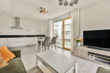 Çağdaş dairenin geniş odasındaki dinlenme odası ve mutfağın yakınındaki sandalyeli ve çiçekli masa.